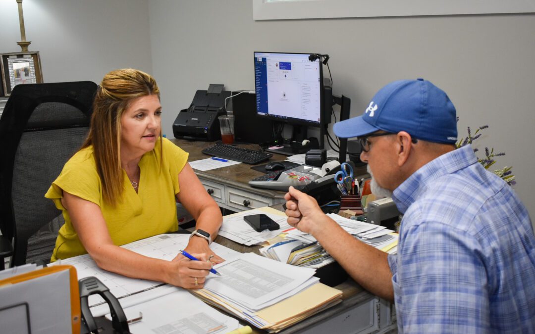 A woman and man seated at a desk, reviewing documents and papers together in a professional setting.