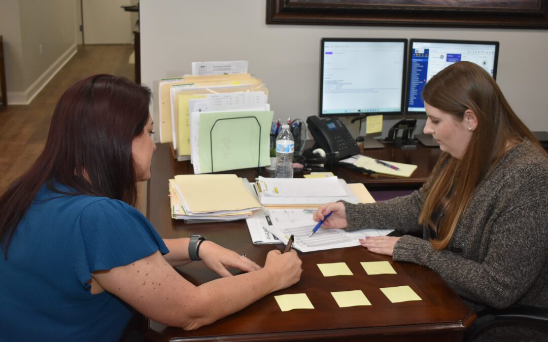 Two women from the Estess CPA Team collaborate at a desk filled with papers and sticky notes.