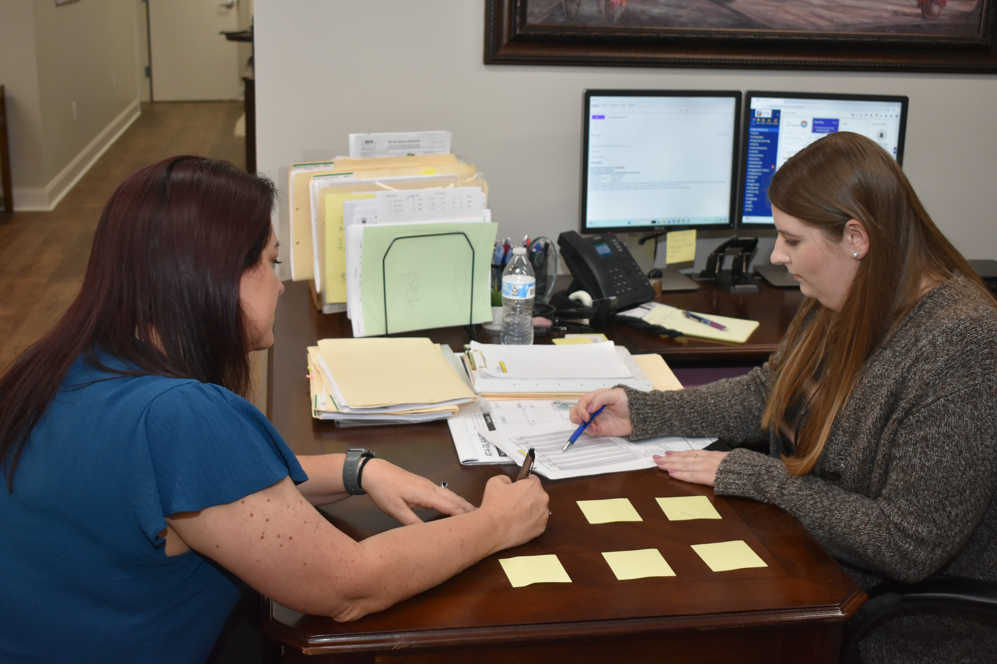 Two women from the Estess CPA Team collaborate at a desk filled with papers and sticky notes.